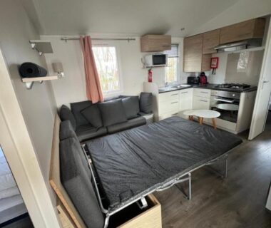 Salon avec banquette déployée et kitchenette dans le Mobil Home Litteau Calvados