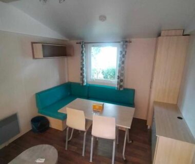Coin repas avec banquette turquoise et fenêtre dans le Mobil-Home Location de Vacances