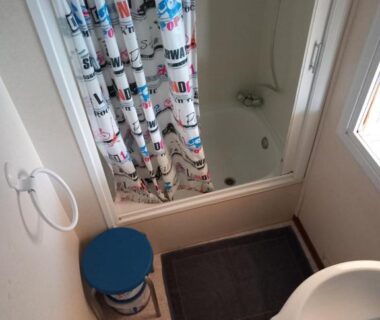 Salle de bains avec baignoire douche et tabouret bleu dans le mobil-home The Duck