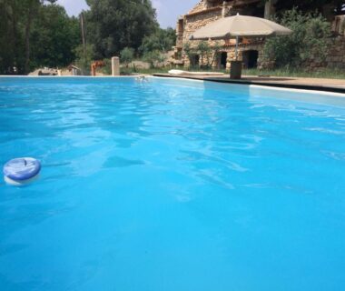Piscine extérieure avec parasol et bâtisse en pierre au Mobil Home à la ferme
