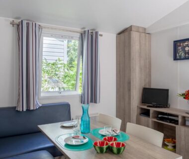Intérieur avec coin repas canapé et télévision dans le Mobil Home sur camping avec piscine