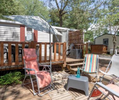 Terrasse en bois avec chaises longues et table du Mobil Home sur camping avec piscine