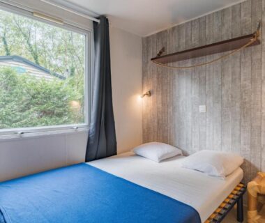 Chambre avec deux lits couverture bleue et fenêtre sur verdure dans le mobil-home