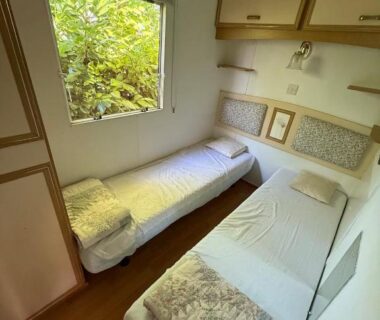 Chambre intérieure avec deux lits et fenêtre sur végétation dans le mobil-home