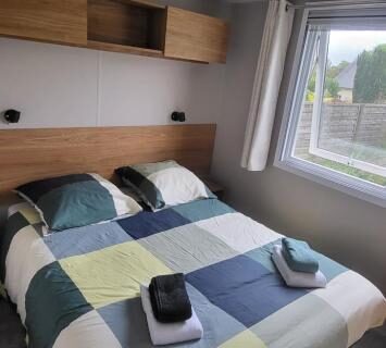 Chambre avec lit double et serviettes près de la fenêtre dans le mobil-home 28 m2