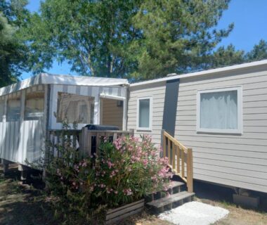 Terrasse ombragée et façade entourée de pins du mobil-home 3 chambres