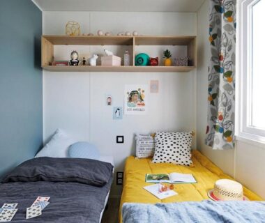 Chambre avec deux lits, étagères et rideaux fleuris dans le Mobil home 3 chambres du Domaine du Vieux Moulin