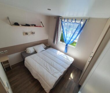 Chambre avec lit double et rideau bleu dans le mobil-home 3 chambres climatisé Rivages des Landes
