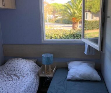 Intérieur chambre avec deux lits et fenêtre donnant sur palmier du mobil home 4 personnes Port la nouvelle