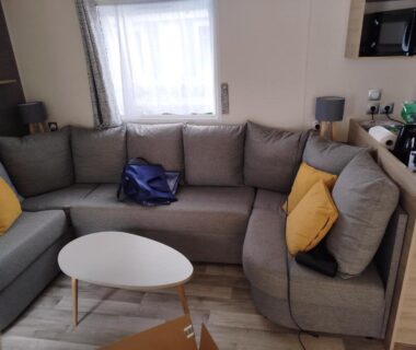 Salon avec canapé d'angle gris et coussins jaunes dans le mobil-home 40m2