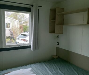 Chambre intérieure avec lit et fenêtre donnant sur le camping du Mobil home
