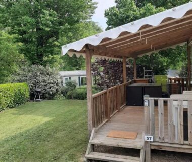 Terrasse couverte en bois avec pelouse et arbres au mobil home