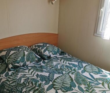 Chambre avec lit double et couette à motifs feuilles dans le mobil-home