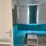 Coin salon avec banquette turquoise et table dans le mobil home 6 pers camping 5