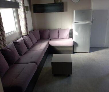 Coin salon avec canapé d'angle violet et frigidaire dans le Mobil-home 6 personnes Camping 4 etoiles