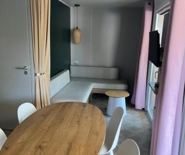 Salon avec table en bois chaises banquette et télévision dans le Mobil home 6 personnes à 400m de la mer