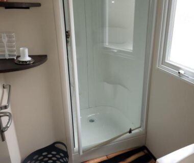 Salle d'eau avec cabine de douche fenêtre et panier à linge dans le mobil home Les Dunes de Contis