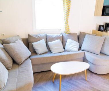 Salon avec canapé d'angle et table basse dans le mobil-home 6/8 personnes du Camping Siblu Domaine de Dugny