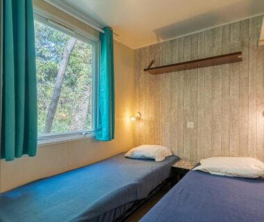 Chambre avec deux lits simples et fenêtre sur les arbres dans le mobil-home