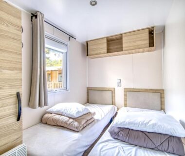 Chambre avec deux lits et placard près de la fenêtre dans le mobil home Amira 42m2