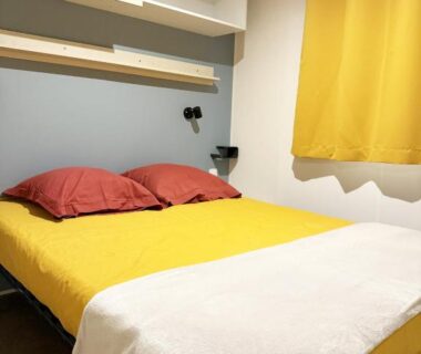 Chambre avec lit double coussins rouges et rideau jaune dans le mobil-home Camping Le Marisol à Torreilles-plage