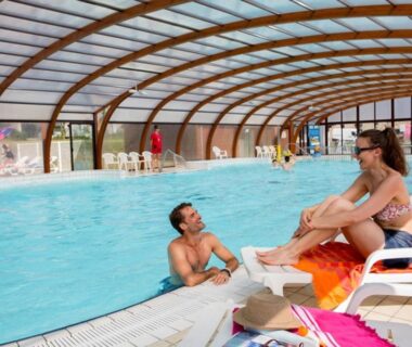Piscine couverte avec homme dans l'eau et femme sur transat au Mobil home Céleste 6-8 personnes