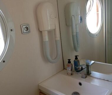 Salle de bains avec lavabo miroir hublot et sèche-cheveux du mobil home Chrisali