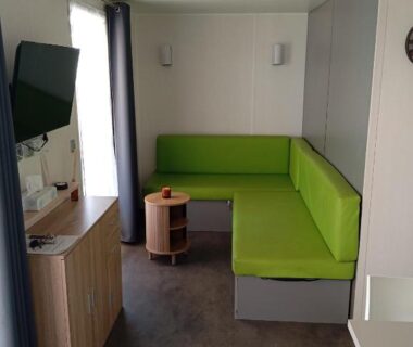 Intérieur salon avec banquette d'angle verte et télévision dans le Mobil home Chrisali