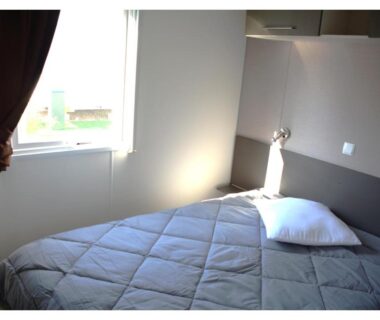 Chambre avec lit, fenêtre et lampe dans le mobil home MH-A004 du Camping LA CARABASSE