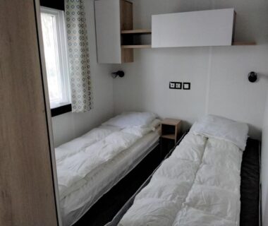 Chambre avec deux lits simples et une fenêtre dans le mobil-home MH-A020 au Camping LE LAC DES RÊVES