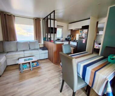 Intérieur du mobil-home avec canapé coin repas et kitchenette dans le Mobil-home Clim MH-A017 du Camping LES OYATS