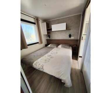 Intérieur chambre avec lit double et fenêtre dans le mobil-home Clim MH-A017 du Camping LES OYATS