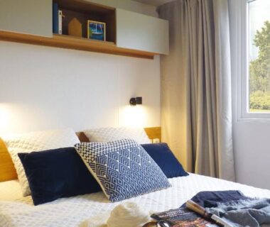 Chambre avec lit et coussins près de la fenêtre dans le Mobil-home Dan Dom