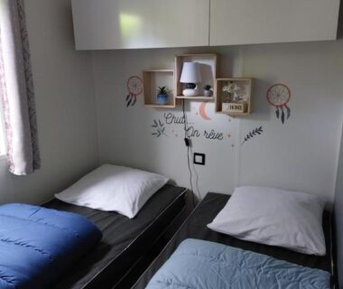 Chambre intérieure avec deux lits et étagères dans le mobil-home La Perle Bleue
