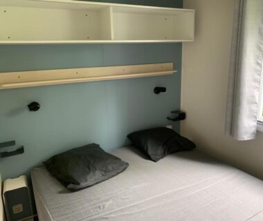 Chambre avec lit double lampes murales et fenêtre dans le mobil-home Ouistreham