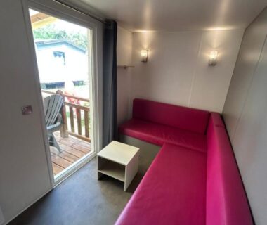 Salon avec banquette fuchsia et terrasse visible du Mobil home Parc des 7 Fonts Les Cigales 4 pers