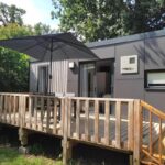 Terrasse extérieure avec parasol et chaises du mobil home TAOS Luxe H20 au Camping de Lanniron