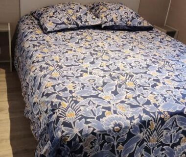 Chambre avec lit double tête de lit blanche et couvre-lit bleu dans le Mobil-home alex