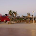 Esplanade bordée de parasols en paille et d'un bus rouge au Mobil home au castellas marseillan