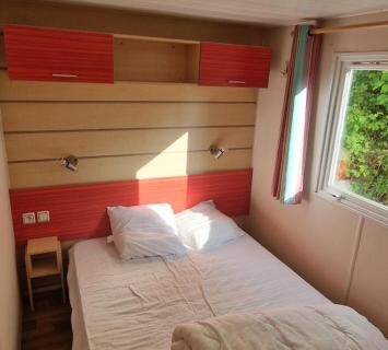 Intérieur de la chambre avec lit double et fenêtre du Mobil-home avec grande terrasse