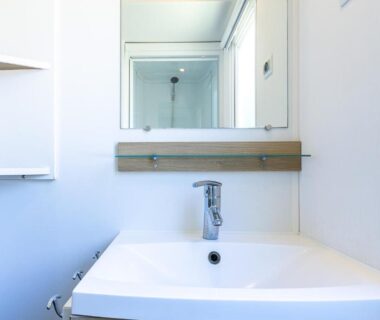 Salle de bain avec lavabo miroir et douche visible dans le reflet du Mobil home camping siblu