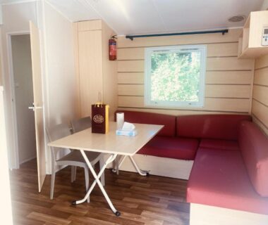 Coin salon avec banquette rouge et table dans le mobil-home climatisé à 5 min de la mer charmant