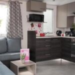 Salon avec kitchenette et canapé dans le Mobil home famille Calazel