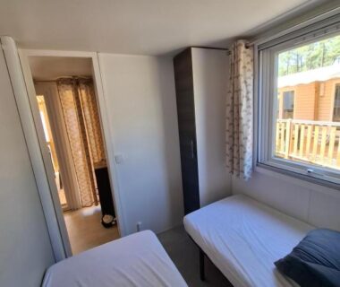 Chambre avec deux lits et fenêtre donnant sur la terrasse du Mobil home les Embruns