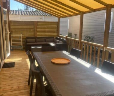 Terrasse couverte avec grande table et canapé du mobil-home neuf 6 à 8 pers au Camping Les Palmiers