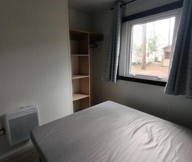 Chambre avec lit et fenêtre dans le mobil-home neuf sous les pins