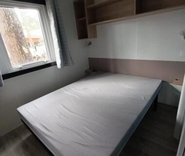 Chambre avec lit double et fenêtre donnant sur l'extérieur du Mobil-home neuf sous les pins