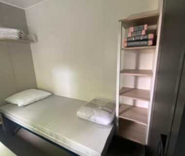Chambre compacte avec lit simple et étagère dans le mobil home plage 4 étoiles