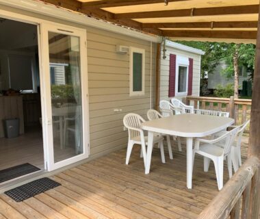 Terrasse en bois avec table et chaises devant baie vitrée du Mobil home près de l étang