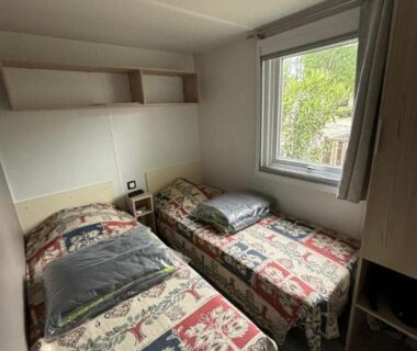 Chambre avec deux lits simples et fenêtre sur végétation dans le mobil home tout confort Camping la falaise